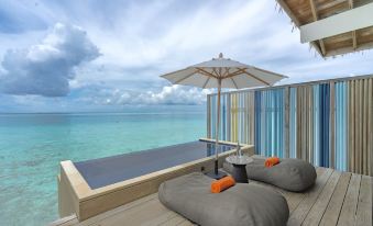 a balcony overlooking the ocean , with two lounge chairs and an umbrella placed on it at Hard Rock Hotel Maldives