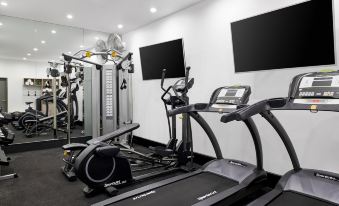 a gym with multiple treadmills , stationary bikes , and other exercise equipment , including a television mounted on the wall at ValueSuites Green Square