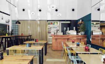 a modern café interior with wooden tables , chairs , and a bar area , decorated in white walls and blue accents at Saint Kilda Beach Hotel, an EVT hotel - Formerly Rydges St Kilda