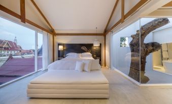 a spacious bedroom with a large bed and white walls , overlooking a balcony with a view of the city at Sala Ayutthaya