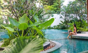 A man swims in a pool surrounded by lush tropical plants and shrubbery at Hotel Vellita Siem Reap