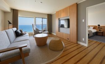 a living room with a large flat - screen tv mounted on the wall , surrounded by furniture such as a couch , chairs , and a coffee at Oiso Prince Hotel