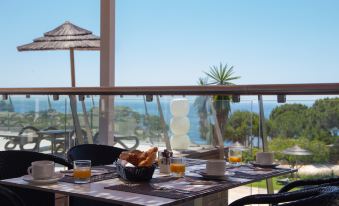 a table with breakfast items is set up on a balcony overlooking the ocean , with a view of the ocean in the background at Vila Alba Resort