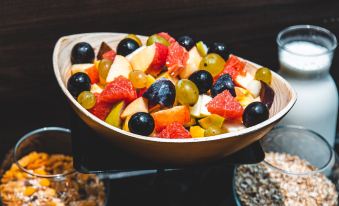 a wooden bowl filled with a variety of fresh fruits , including apples , oranges , and grapes at Mark Hotel Belgrade