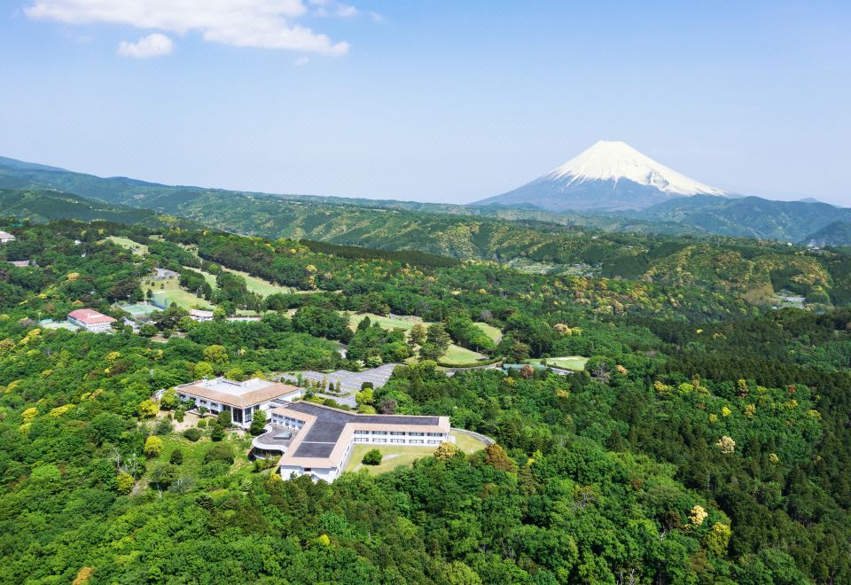 a lush green valley with a snow - capped mountain in the background and a large building surrounded by trees at Izu Marriott Hotel Shuzenji