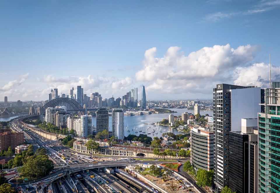 a city skyline with skyscrapers and a large body of water , under a clear blue sky at Meriton Suites North Sydney