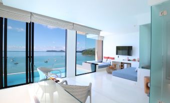 a luxurious living room with large windows offering a view of the ocean , white furniture , and blue cushions at Bandara Villas, Phuket