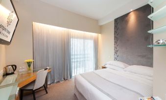The bedroom features a double bed, a desk, and a chair positioned in front of a large window with a view of the surroundings at Empire Hotel Kowloon－Tsim Sha Tsui