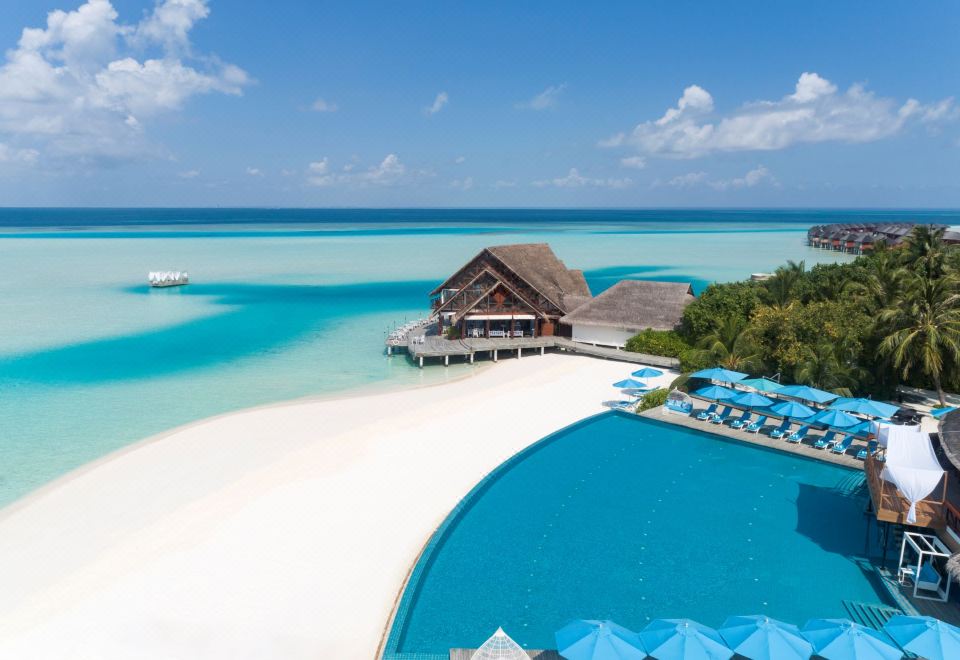 a resort with a large pool surrounded by lounge chairs and umbrellas , as well as a sandy beach in the background at Anantara Dhigu Maldives