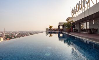 a large swimming pool is seen in the foreground with a city skyline in the background at Louis Kienne Hotel Simpang Lima