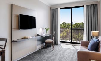 a modern living room with a large window , a couch , and a flat - screen tv . also a dining table nearby at Oaks Sydney North Ryde Suites