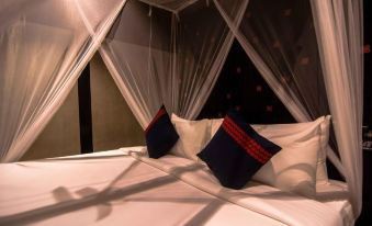 a bed with white sheets and a black canopy , topped with two red and blue pillows at Santani Wellness Kandy