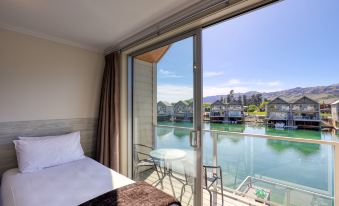 a bedroom with a bed and a sliding glass door leading to a balcony overlooking water at Marsden Lake Resort Central Otago