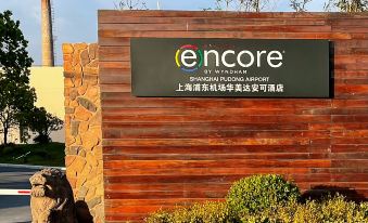 A building's entrance with signage and an outdoor seating area in front on a sunny day at Ramada Encore by Wyndham Shanghai Pudong Airport