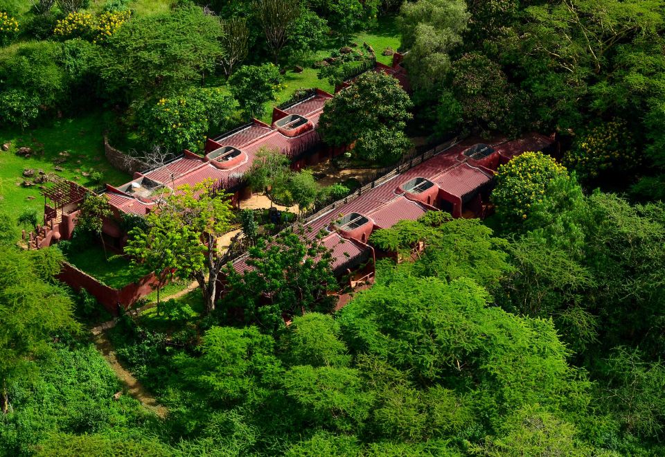 a lush green forest surrounds a red - roofed building , with the same building situated in the same location as a restaurant at Amboseli Serena Safari Lodge