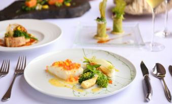 a white plate with a piece of fish , broccoli , and carrots on a dining table at Sankara Hotel & Spa Yakushima