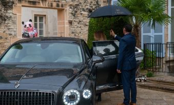 a man in a blue suit is holding an umbrella while standing next to a black car at L'Hotel de Beaune