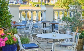an outdoor dining area with white tables and chairs , surrounded by lush greenery and a body of water at Small Luxury Hotels of the World - the Mitre Hampton Court