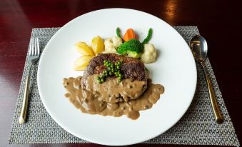 a plate of food on a dining table , consisting of a piece of steak , mashed potatoes , and various vegetables at Lbn Asian Hotel