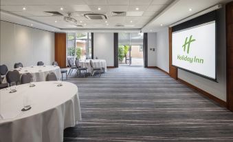 a conference room with tables and chairs , a large screen displaying the holiday inn logo at Holiday Inn Gloucester - Cheltenham