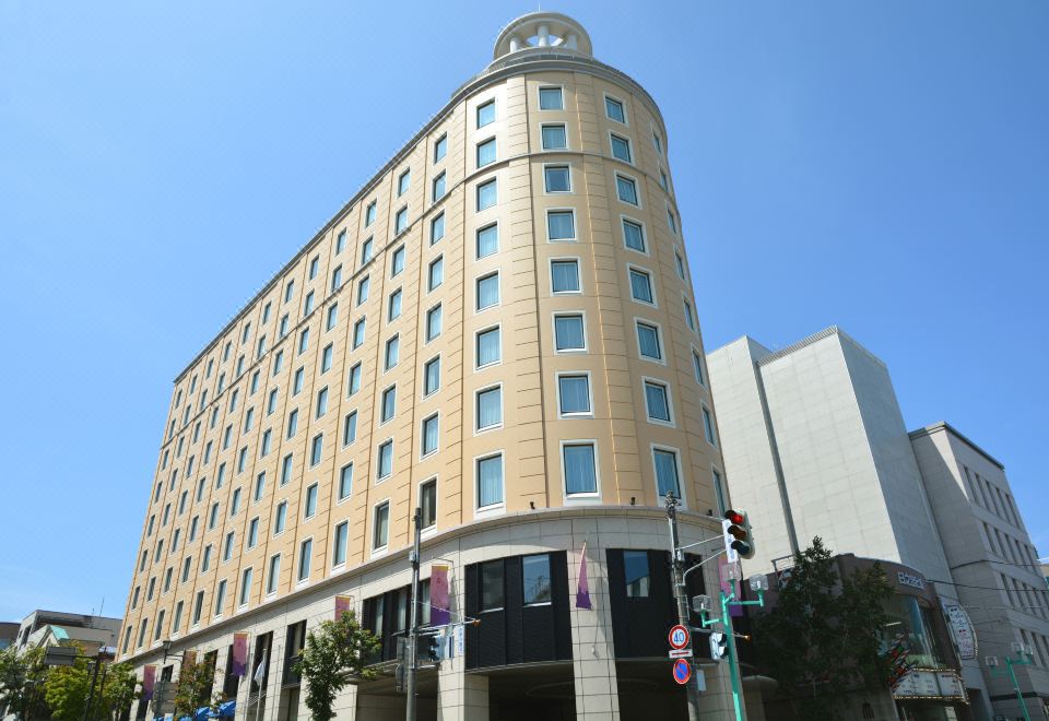 a tall hotel building with a dome on top , located in a city setting with trees and traffic at Authent Hotel Otaru