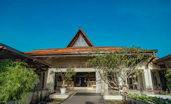 a traditional thai - style building with a red - tiled roof , surrounded by lush green trees and a clear blue sky at Pelangi Beach Resort & Spa, Langkawi
