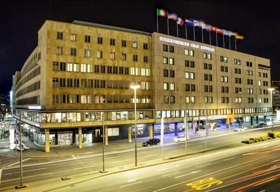 a large building with flags flying in front of it , illuminated at night with street lights at Steigenberger Graf Zeppelin