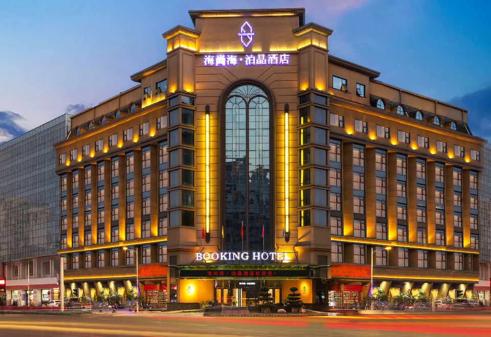 a large hotel building surrounded by trees and other buildings , with lights illuminating the structure at Mianyang Booking Hotel