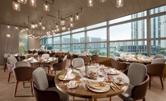 The restaurant features spacious dining room with large windows and tables, providing a picturesque view of the sea at Nina Hotel Tsuen Wan West