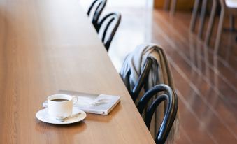 a wooden dining table with a cup of coffee , a newspaper , and two chairs placed on it at Mitsui Garden Hotel Okayama