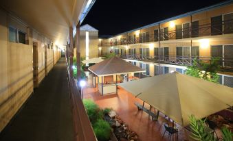 a nighttime scene of an outdoor courtyard with a dining area and several tables and chairs at Stay at Alice Springs Hotel