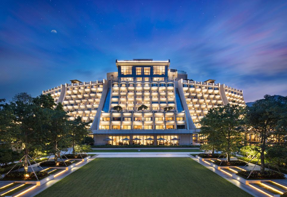 A large building with illuminated lights at night stands in the center, with another hotel situated behind it at Hilton Shenzhen Shekou Nanhai