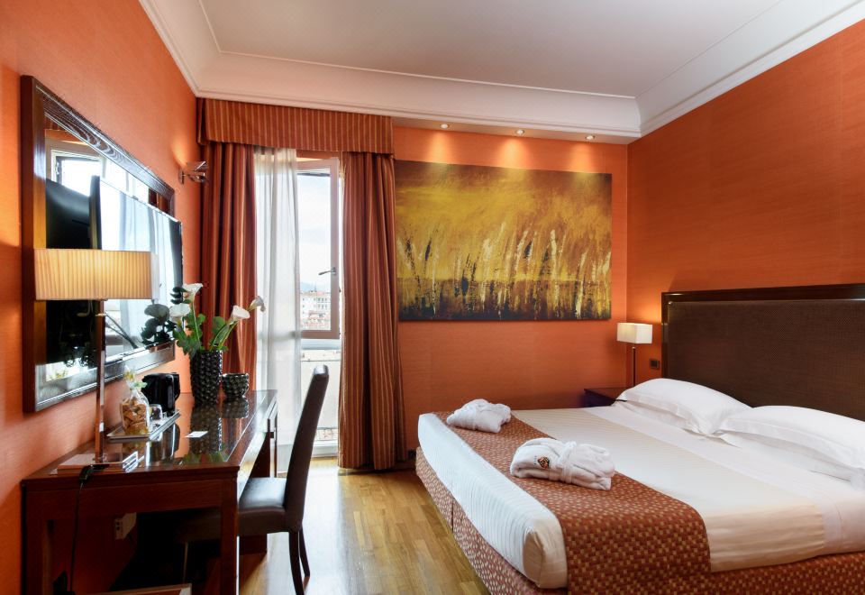 a hotel room with a large bed , desk , and window , decorated with an orange wall and artwork at Grand Hotel Adriatico