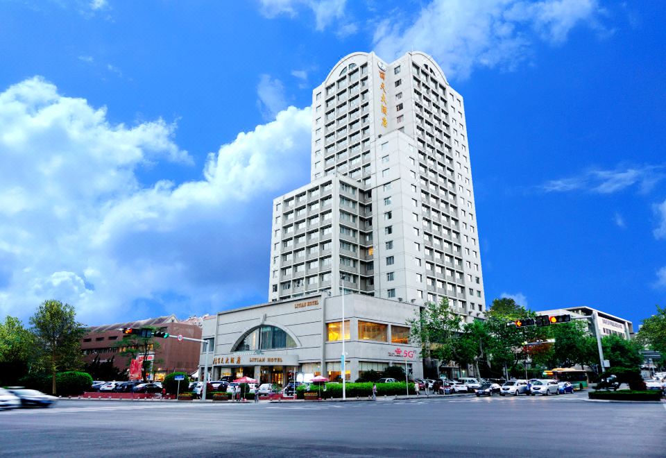 A large building with cars parked in front and streets on both sides at Qingdao  Litian Hotel