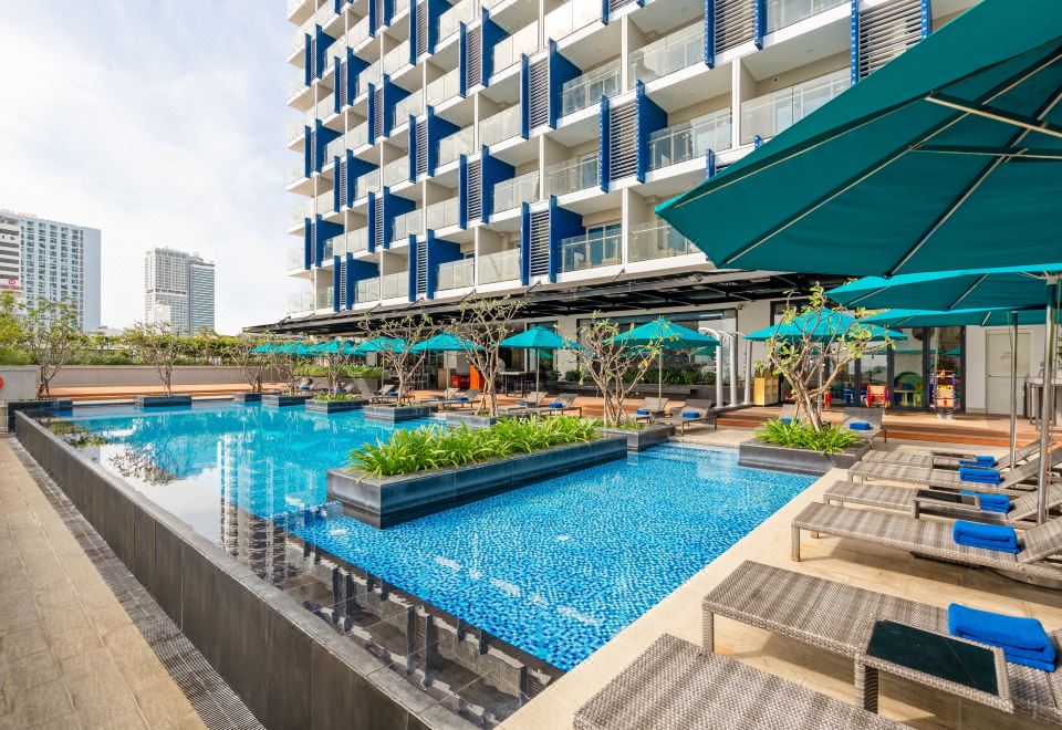 an outdoor pool surrounded by a building , with several lounge chairs and umbrellas placed around the pool area at TUI BLUE Nha Trang