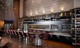 a modern bar with a long counter and several stools , as well as a variety of bottles and wine glasses at Oval Hotel at Adelaide Oval, an EVT hotel