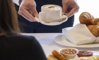 a man is holding a cup of coffee and a plate of food on a dining table at Dorsett Wanchai