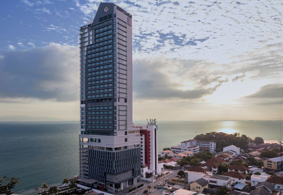a tall building with a glass facade is surrounded by smaller buildings and water , with the sky above at Hompton Hotel by The Beach