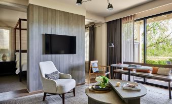 a cozy living room with a white armchair , wooden dining table , and a flat - screen tv mounted on the wall at Rosewood Sand Hill