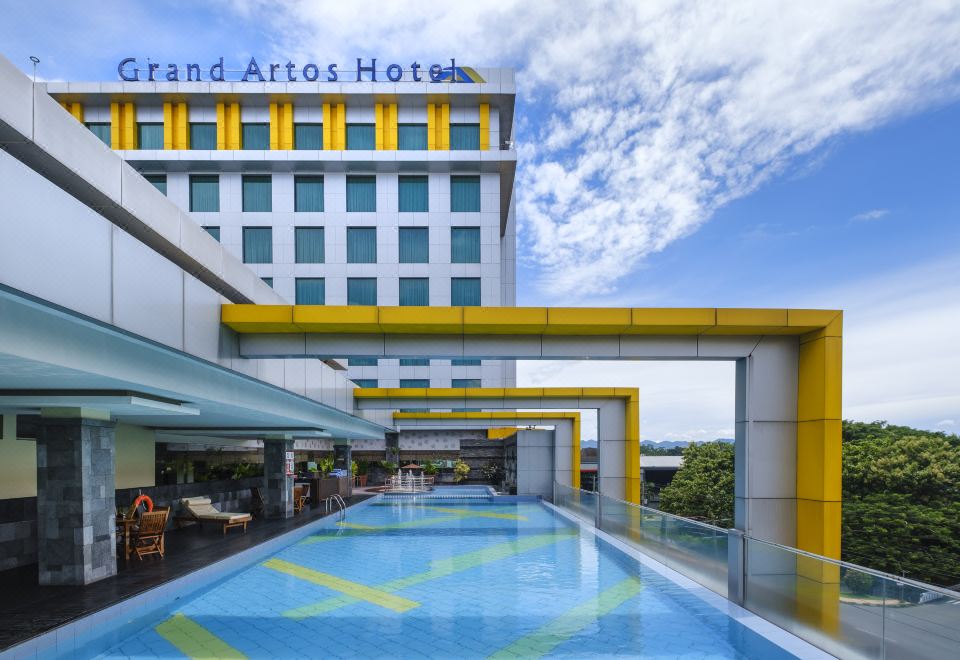 a large hotel with a swimming pool in front of it , surrounded by trees and grass at Grand Artos Hotel & Convention
