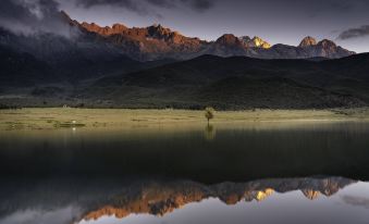 a serene scene with a lone tree in the middle of a lake , surrounded by mountains at The Rock Hotel