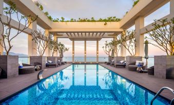 a large swimming pool with a pergola and lounge chairs is surrounded by water and trees at Paris Deli Danang Beach Hotel