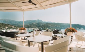 an outdoor dining area with a view of the ocean , featuring white chairs and tables at Jumeirah Port Soller Hotel and Spa