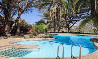 a large outdoor swimming pool surrounded by palm trees and lush greenery , with a staircase leading into the pool area at Amboseli Serena Safari Lodge
