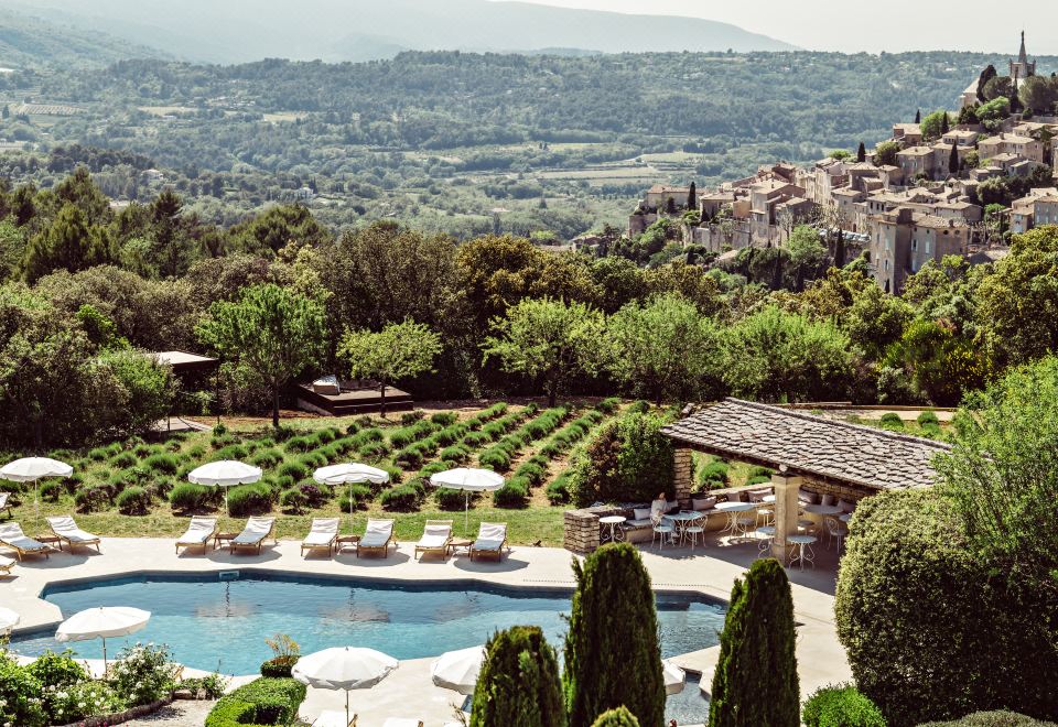 a beautiful outdoor pool area with umbrellas , sun loungers , and lush greenery surrounding a picturesque landscape at Capelongue, a Beaumier Hotel & Spa
