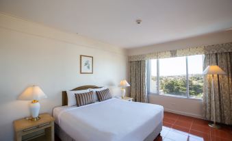 a hotel room with a white bed , curtains , and a window , providing a view of the city at The Imperial Narathiwat Hotel