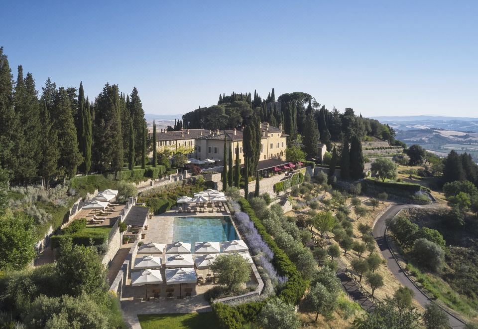 an aerial view of a resort with a large pool surrounded by trees and buildings at Rosewood Castiglion del Bosco