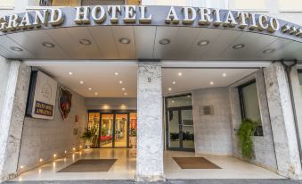 "a modern hotel entrance with the name "" adriatic "" in black letters , marble pillars , and two entrances decorated with potted plants and car" at Grand Hotel Adriatico