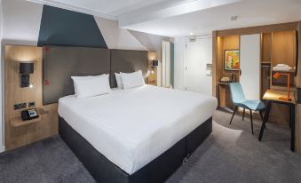 a large bed with white linens is in a room with a blue chair and a framed picture at Holiday Inn Gloucester - Cheltenham
