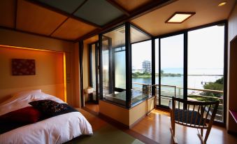 a luxurious bedroom with a large bed , a bathtub in the corner , and a view of a lake outside the window at Biwako Ryokusuitei